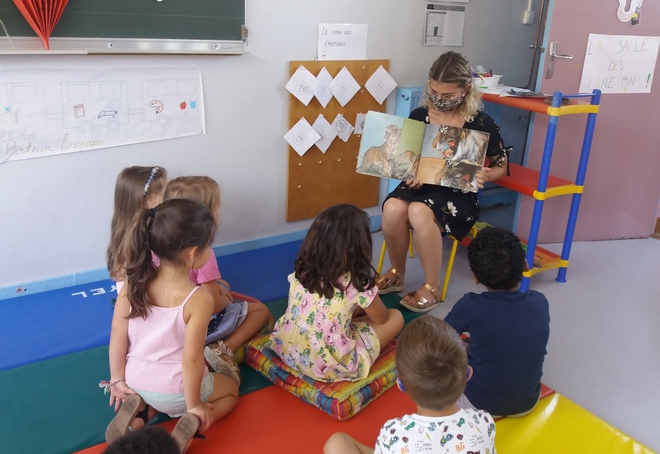 Des enfants sont réunis autour d'une animatrice qui leur lit une histoire