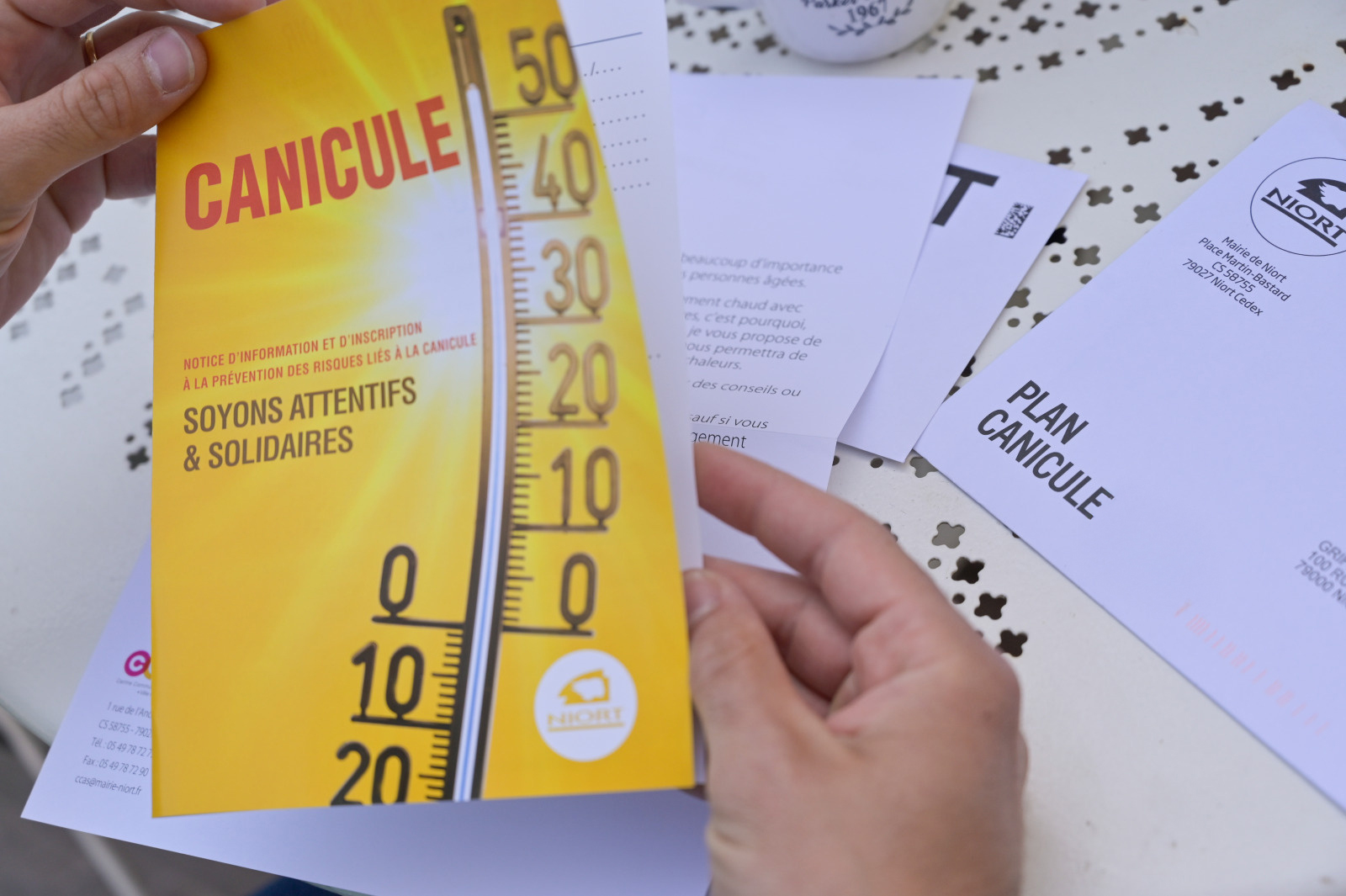 Brochure Plan Canicule de la Ville de Niort tenue en main, avec thermomÚtre et slogan « Soyons attentifs & solidaires »