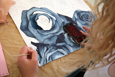 Élève réalisant une aquarelle de roses aux teintes bleues et grises, smartphone posé sur l'œuvre comme référence