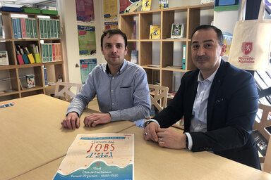 Deux représentants posent dans les locaux d'Info Jeunes Niort avec l'affiche du Forum des jobs d'été sur la table.