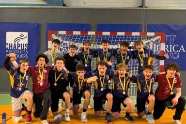 Les joueurs en tenue bleue arborent leurs médailles et célèbrent en groupe devant un but de handball.