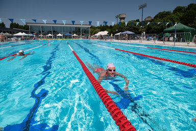 Nageurs dans les couloirs du bassin extérieur en plein soleil, avec le bâtiment de la piscine en fond