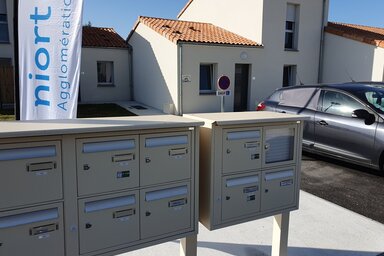 Boîtes aux lettres collectives devant des maisons individuelles neuves, avec la bannière Niort Agglomération